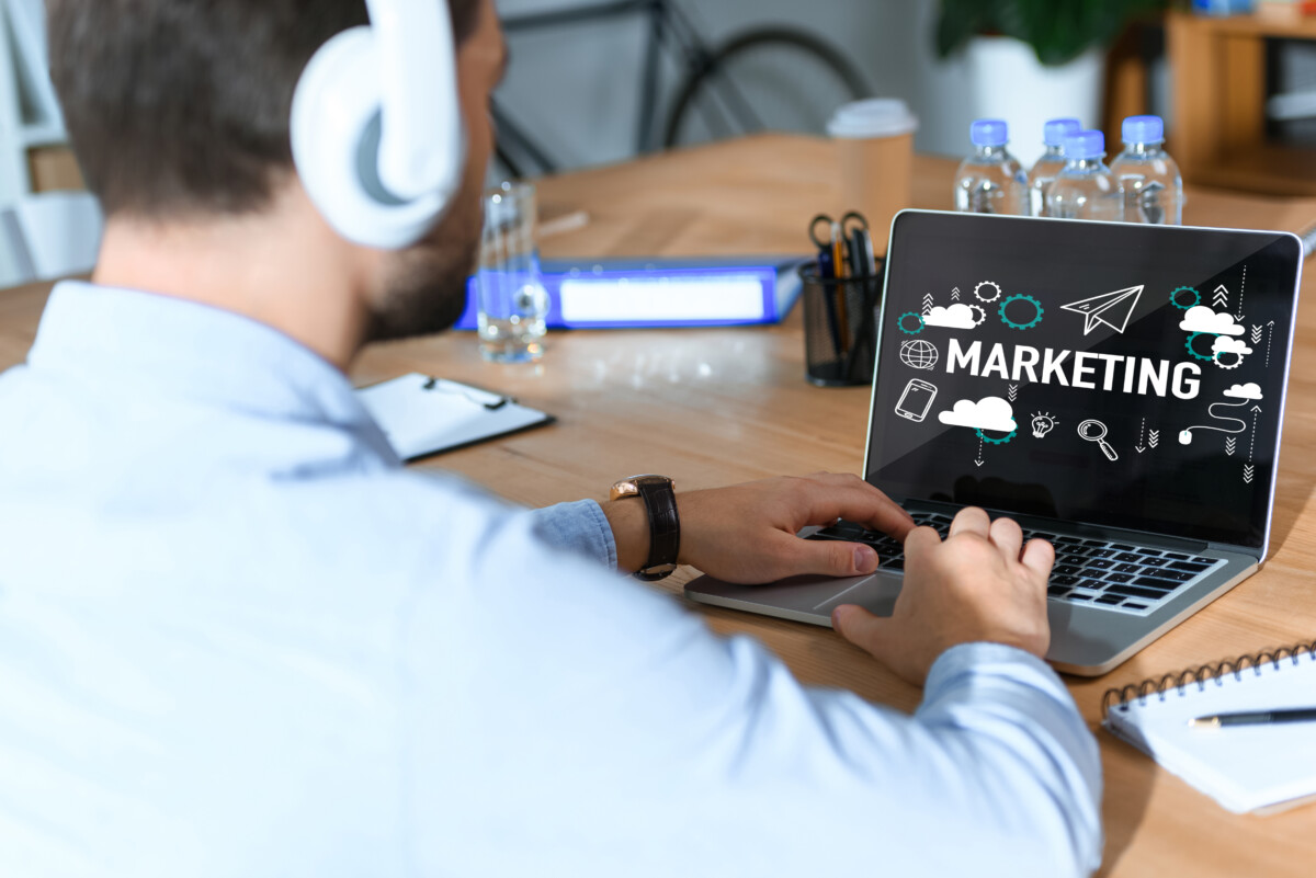 cropped shot of businessman in headphones listening music and working at laptop with marketing word