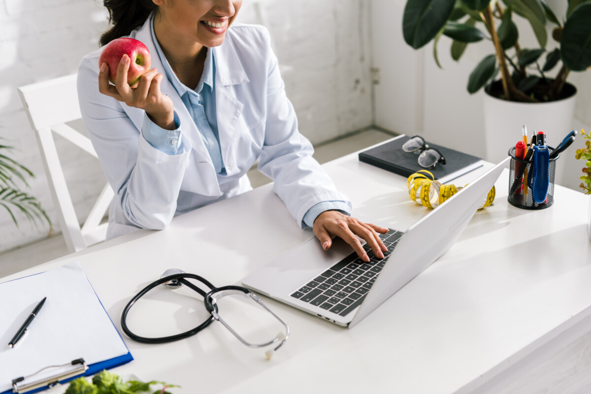 cropped view of happy woman holding apple and typing on laptop