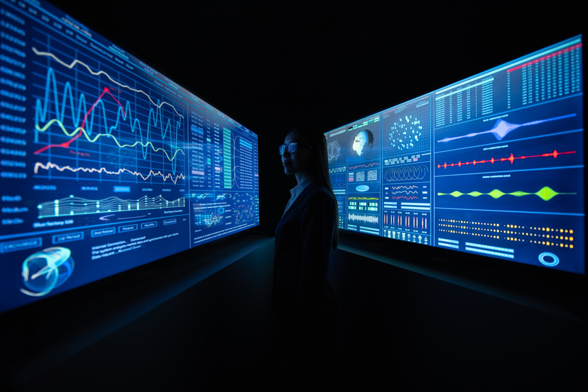 The business lady standing between blue monitors in the dark office.